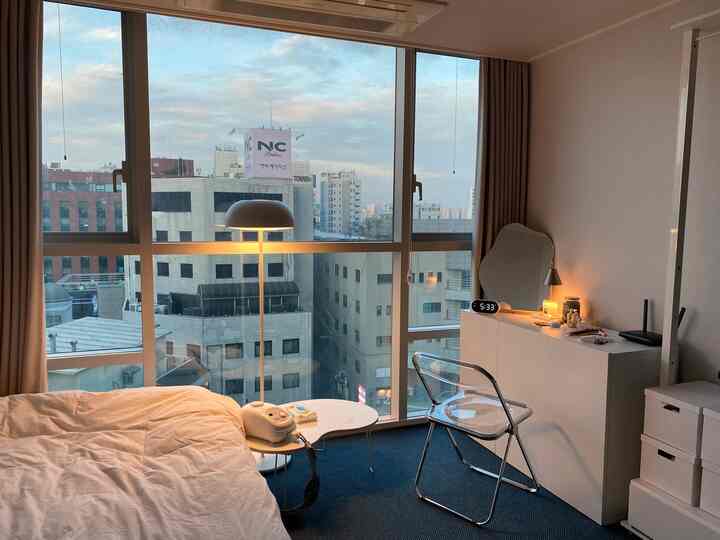 A simple one-person bedroom in white and navy tones featuring a bed, transparent chair, and floor lamp
