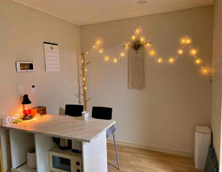 暖かい照明とナチュラルカラーのキッチンアイランドがあるキッチン、ストリングライトとマクラメウォールハンギングで装飾された雰囲気のある空間