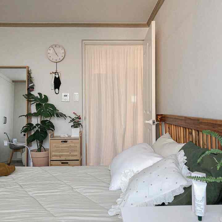 白と茶色のトーンの寝室、木製ベッドと収納キャビネット、植物が配置された自然な雰囲気のあるインテリア