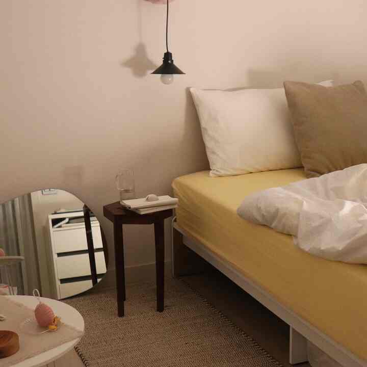 柔らかいホワイトとイエローの色調の寝室、ナイトテーブルとペンダントライトが配置された雰囲気のあるインテリア