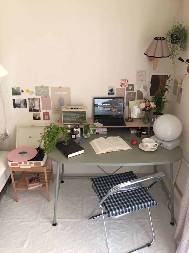 White and green toned studio apartment with vintage style desk, laptop, turntable, and plants creating cozy workspace