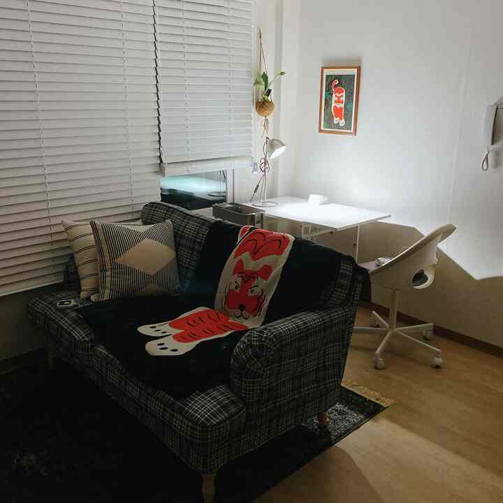 White and wood tone living room combined with a home office, featuring a plaid sofa and a white desk in a cozy atmosphere