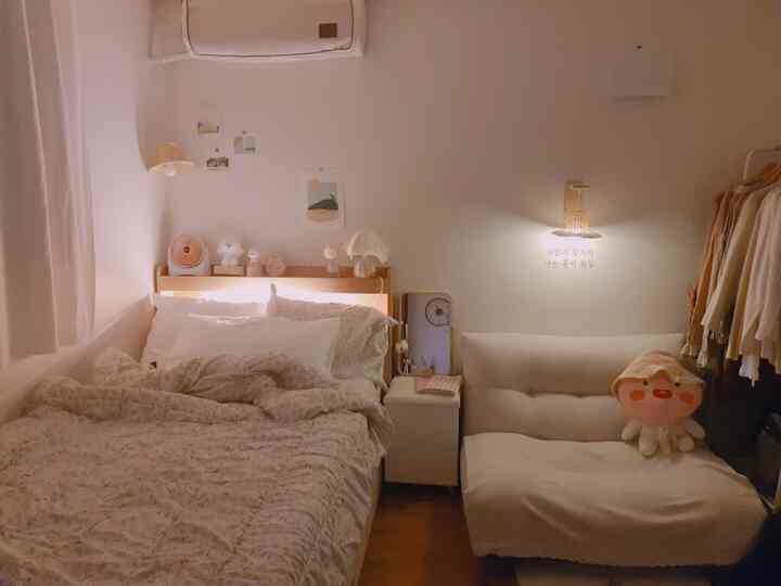 Beige and white toned compact studio bedroom featuring wood-tone bed and white two-seater sofa with cozy ambiance