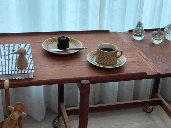 Wood tone table featuring a coffee cup and dessert plate set in a cozy home cafe atmosphere. White chiffon curtains in the background emphasize a warm autumn feel.