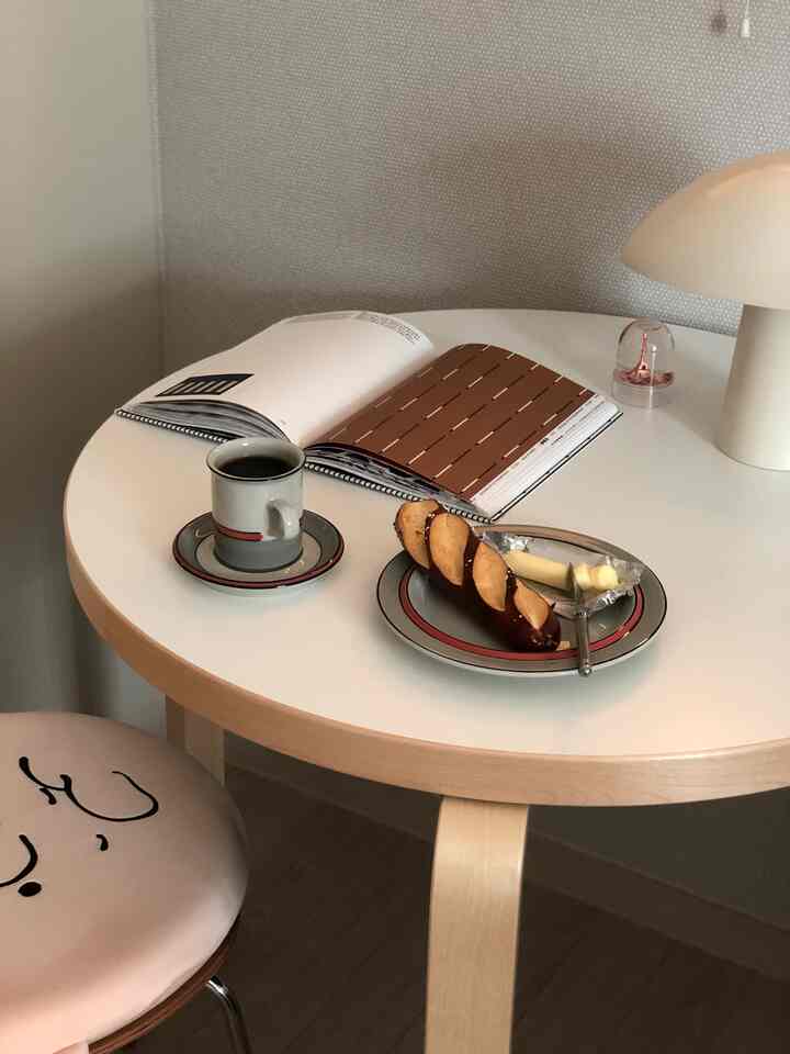 White and natural wood-toned bedroom round table featuring coffee, a book, and a table lamp creating a cozy home cafe spot