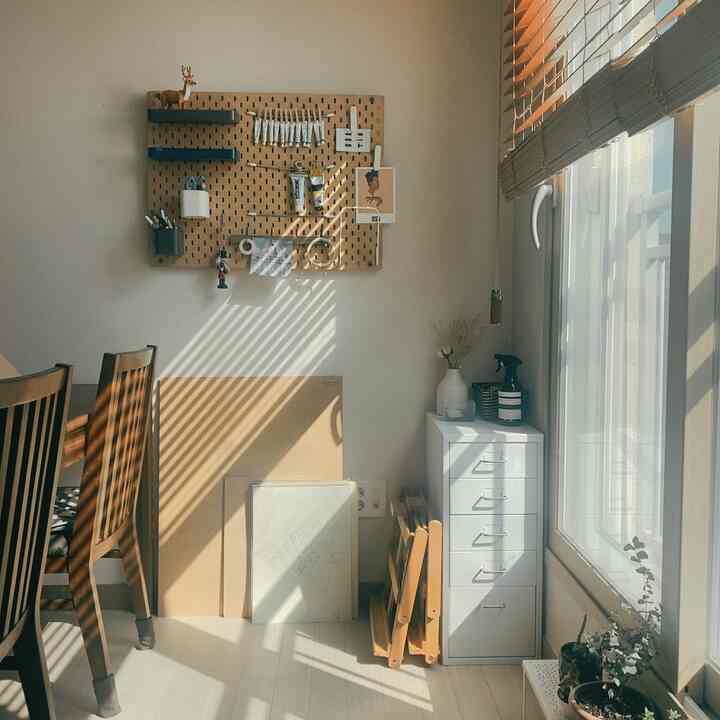Cozy art workspace blending warm wood tones and white, featuring a pegboard and a dresser under natural light