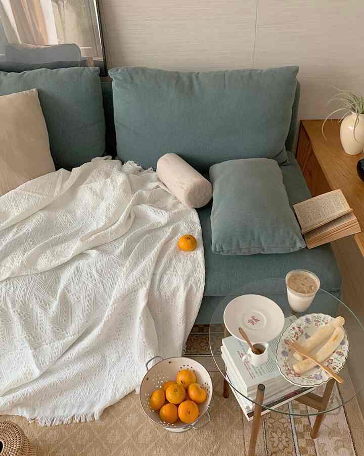 ナチュラルな色調のリビング、ブルーグリーンのソファと白いスロー、みかんとおうちカフェのアイテムが配置された雰囲気あるインテリア