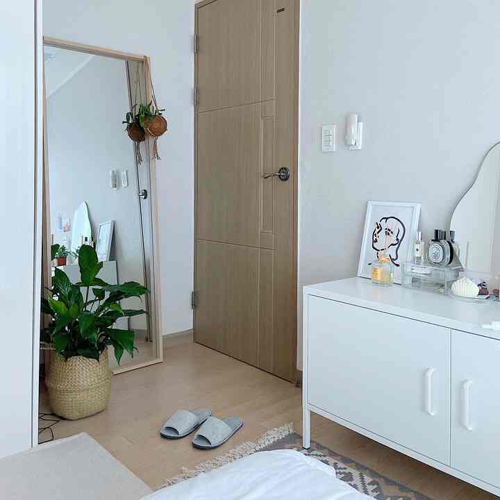 ベージュとホワイトのナチュラルカラーの狭い寝室、扉の後ろの隙間に全身鏡と植物が配置された雰囲気のあるインテリア