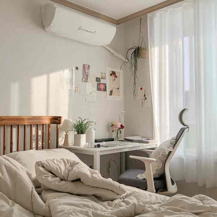 Cozy bedroom in warm beige and white tones featuring a wooden bed and white desk bathed in natural autumn light