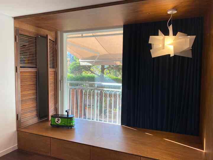 暖かい木目調とダークな遮光カーテンが調和した子供部屋、低い平台とペンダントライトが配置された雰囲気のある空間