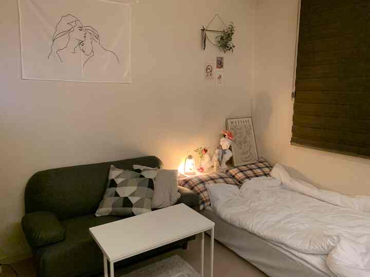 White and gray-toned studio bedroom-living space featuring dark gray sofa and cozy white bed with warm lamp lighting
