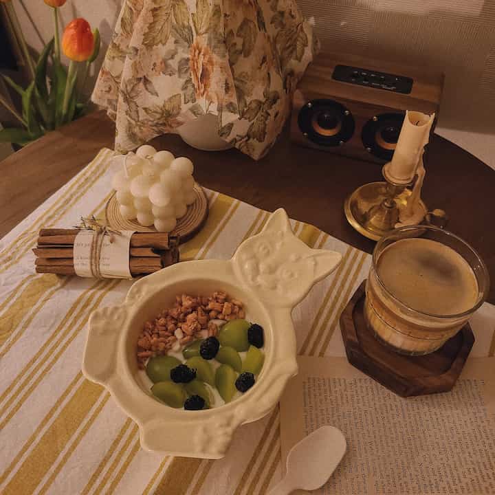 温かみのあるブラウンの木目調テーブルに、ヴィンテージの小物と猫の形の器、コーヒーカップが配置された雰囲気のあるおうちカフェのインテリア