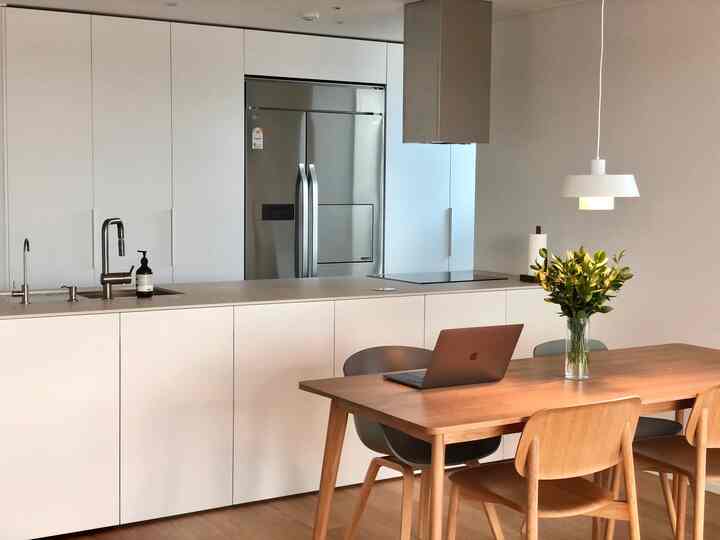 ホワイトと木目調の調和があるキッチンとダイニング、木製のダイニングテーブルと椅子、ペンダントライトが配置された温かみのある空間