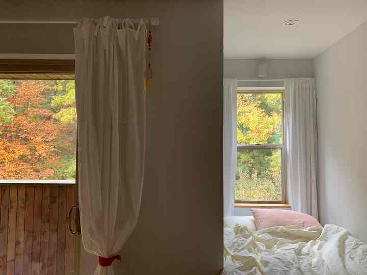 A cozy kids' room in white and beige tones, featuring large windows with curtains framing autumn leaves outside