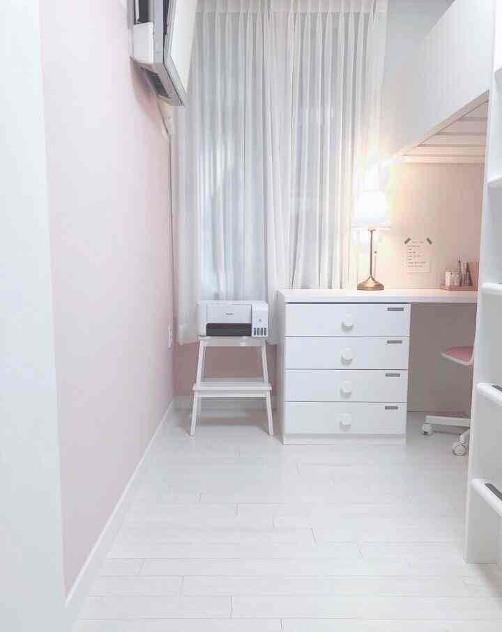 Bright white-toned kids' room with pink accents, featuring a dresser, stool, and table lamp neatly arranged in a cozy space