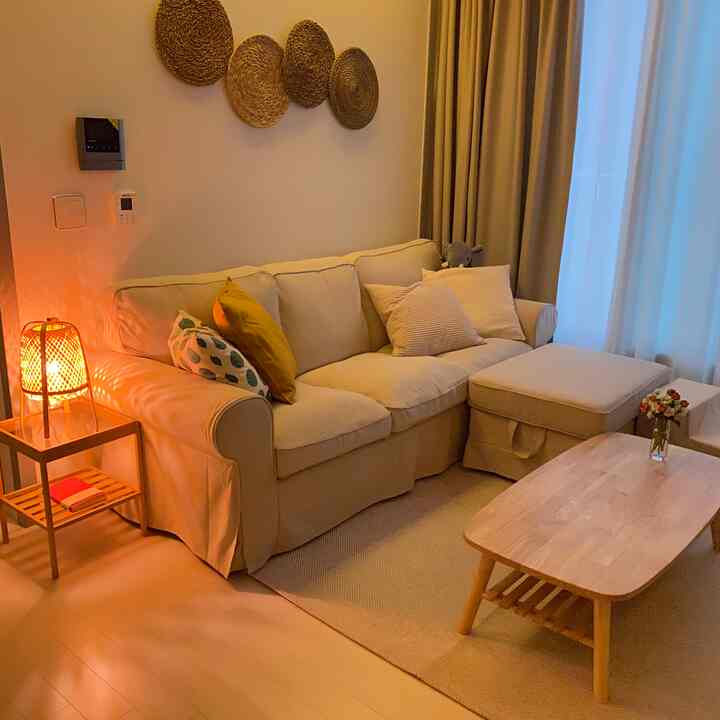 Warm beige-toned living room featuring a beige fabric sofa, wooden coffee table, rattan decor, and ambient lighting creating a cozy atmosphere