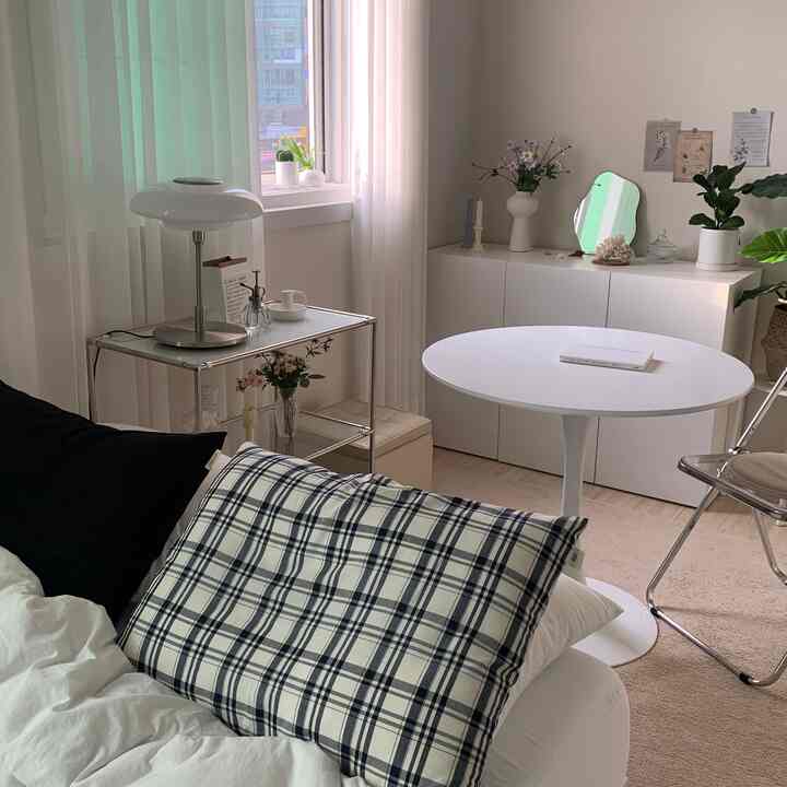 Bright white and beige toned studio bedroom featuring a simple dining table, plants, and cozy atmosphere