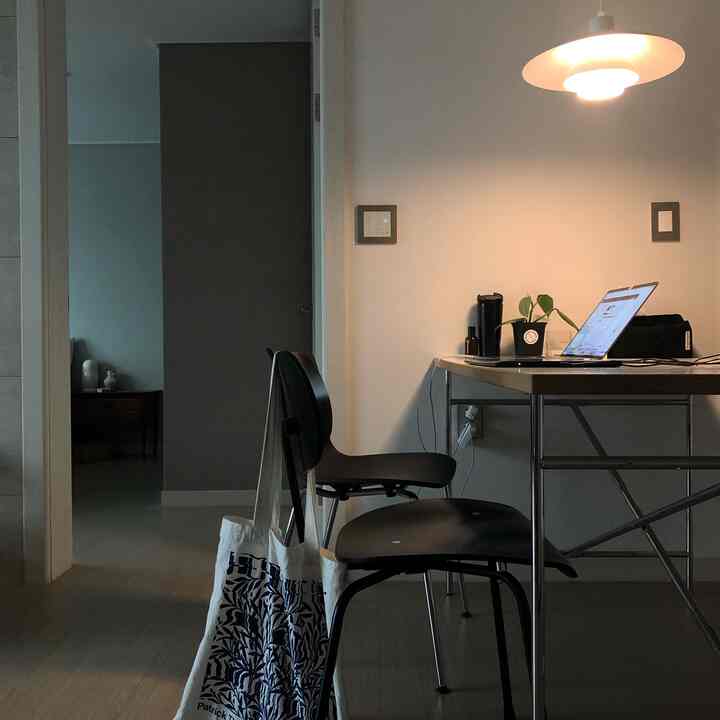 A modern kitchen space with white walls and black furniture, featuring a laptop and plants in a calm remote work setting