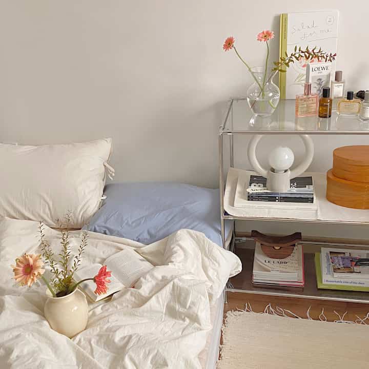 Ivory and beige toned studio bedroom featuring vases and storage shelves with a cozy atmosphere