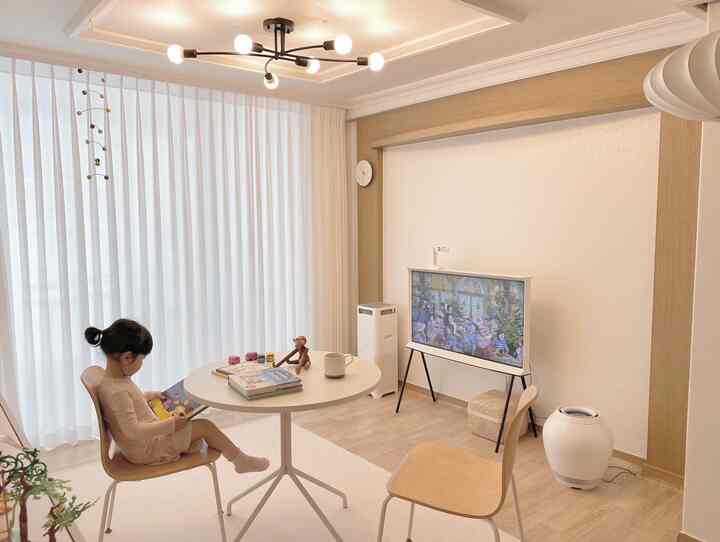 A white and wood tone living room featuring a round dining table and a child reading, creating a cozy atmosphere