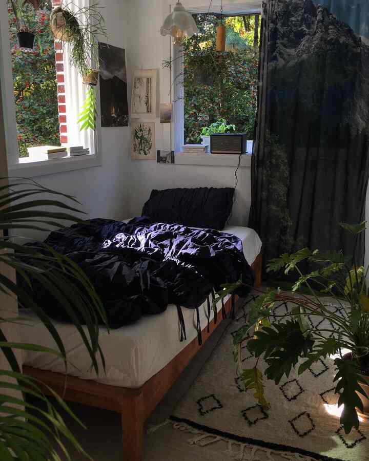 White-walled bedroom with wood tone bed, featuring multiple green plants and artistic posters creating a natural and artistic ambiance