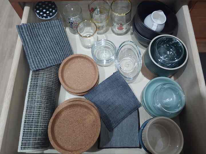 ベージュと透明の色調が特徴のキッチンの引き出し、コースターやソジュグラス、陶器のボウルが整然と配置された雰囲気のあるインテリア