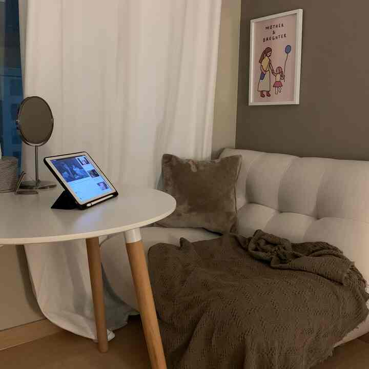 White and wood-toned studio living room featuring a round table and beige sofa with brown blanket and cushion for cozy ambiance