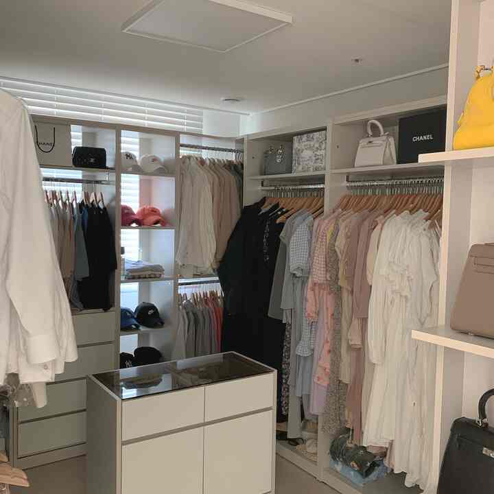 White-toned walk-in closet featuring organized clothes and drawers with a clean interior design