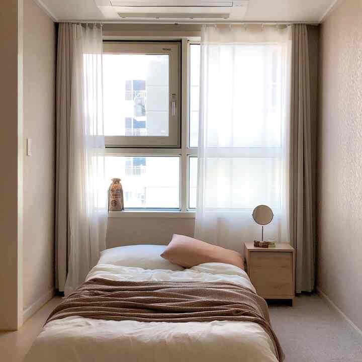 Monotone beige and white small studio bedroom featuring simple bedding and a wooden nightstand creating a cozy space