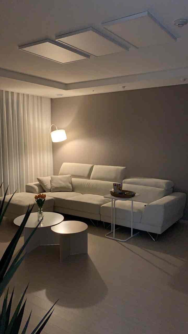 白を基調としたリビング、中央にコーナーソファとフロアランプ、サイドテーブルが配置されたシンプルでモダンなインテリア