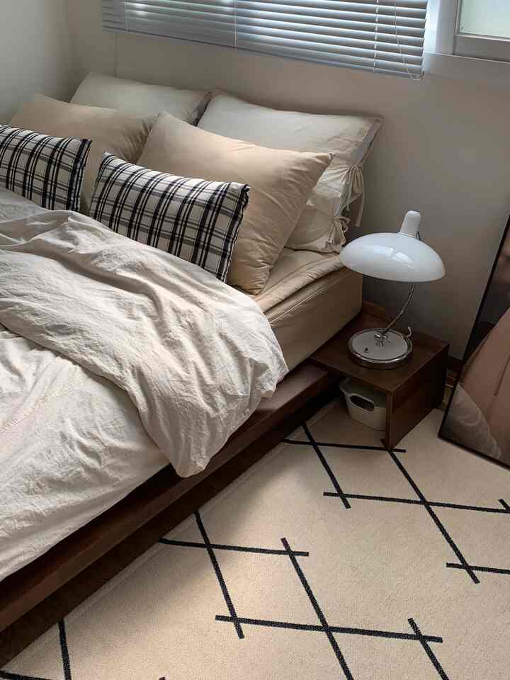 White and beige toned bedroom featuring wood-tone bed and nightstand, patterned rug creating a natural atmosphere
