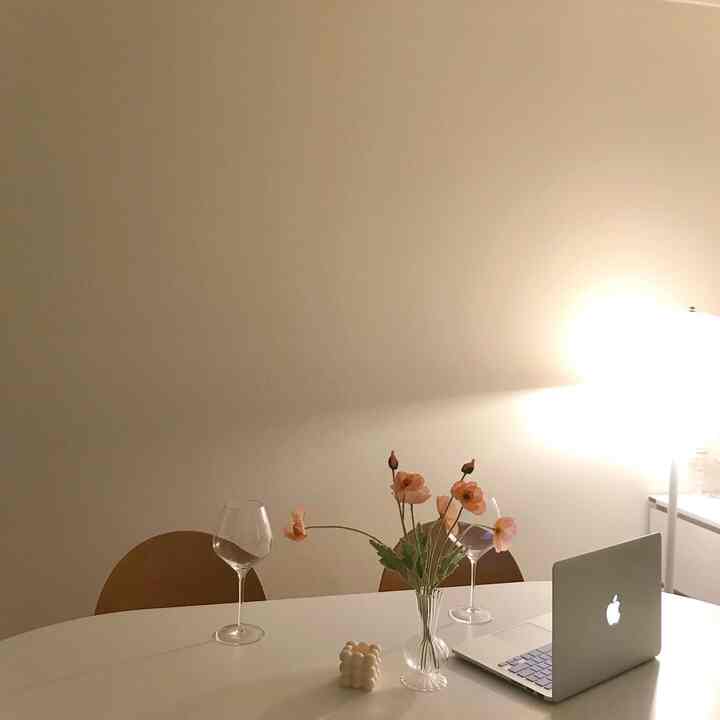 White and beige toned dining room featuring a table with poppy flowers, wine glasses, and a laptop, creating a cozy atmosphere
