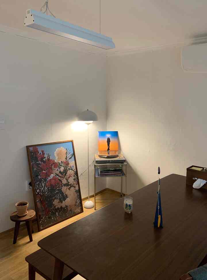 Wood tone and white-toned living room featuring a wooden dining table, floor lamp, and large art piece leaning against the wall creating a cozy atmosphere