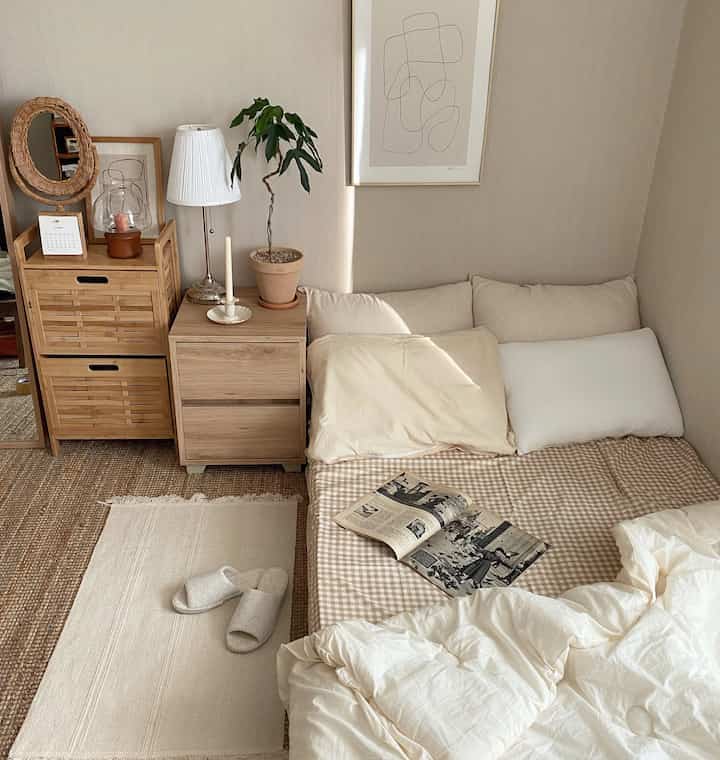 Natural color toned studio bedroom featuring beige checked duvet cover, wood tone nightstand, and potted plant creating cozy atmosphere