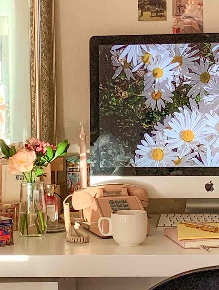 White and beige toned home office featuring a vintage telephone, flowers, and candle objets on a cozy desk