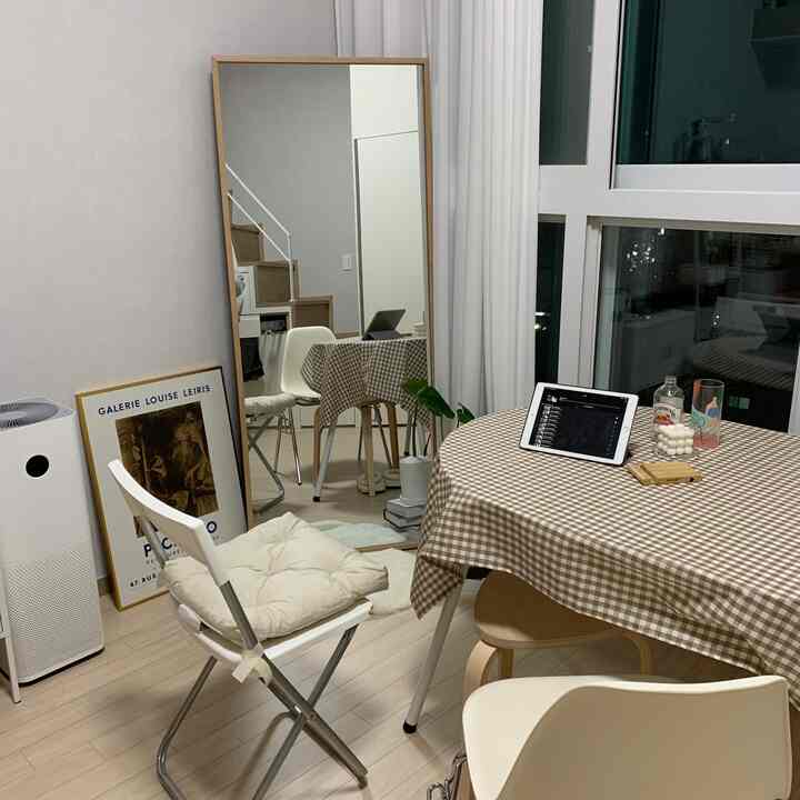 Natural-toned studio dining space in white and beige featuring a checkered tablecloth and full-length mirror with cozy atmosphere