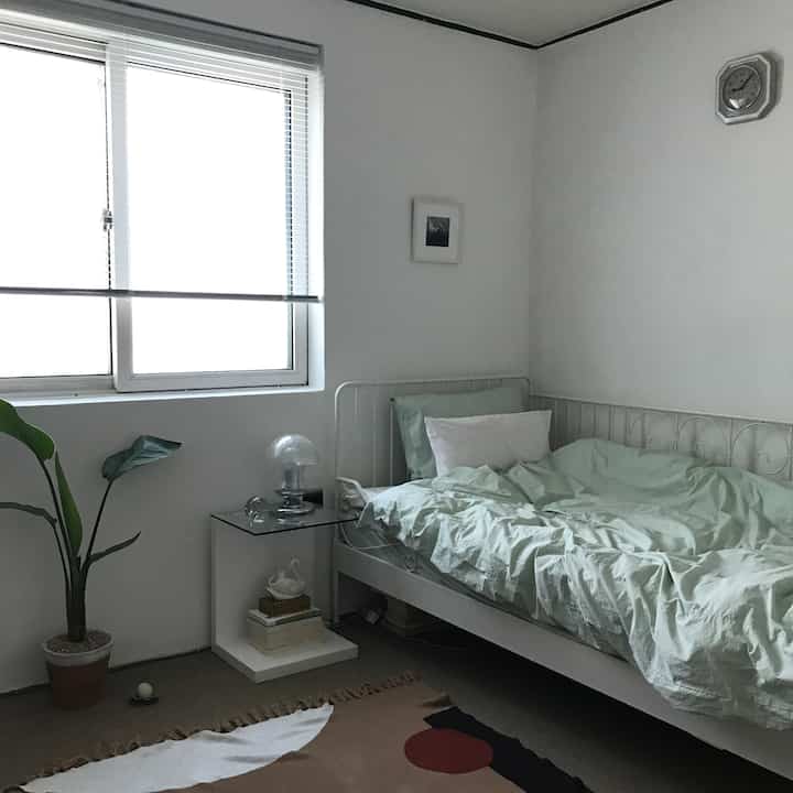White and mint toned small bedroom featuring a bed, side table, and plant with a natural atmosphere