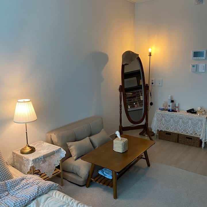 Beige and brown toned compact living room featuring sofa, wooden coffee table, full-length mirror, and warm lighting creating cozy atmosphere