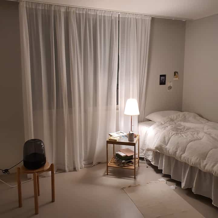 White and natural-toned bedroom featuring a white bed, chiffon curtains, bamboo side table, and floor lamp creating a warm atmosphere