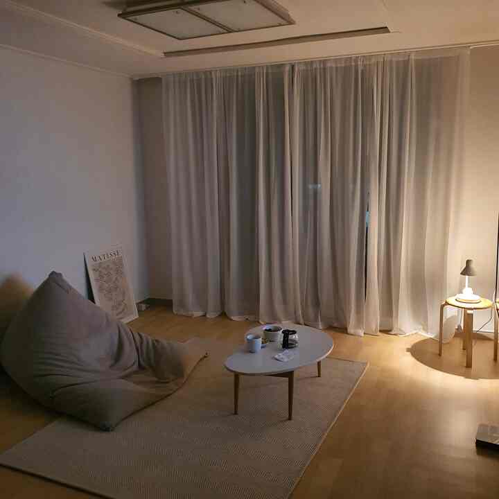 Beige and natural toned living room featuring a bean bag sofa, coffee table, and sheer curtains creating a cozy atmosphere
