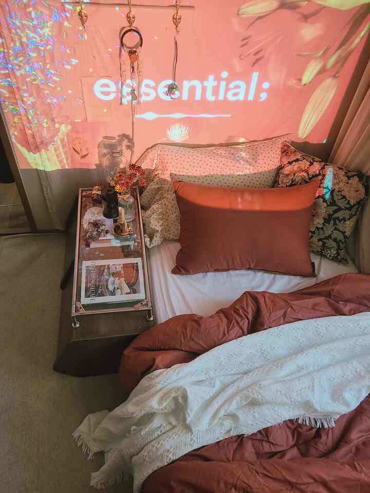 ヴィンテージ感のあるワンルーム寝室、赤みがかった寝具とナイトテーブル、ファブリックが調和した暖かなインテリア