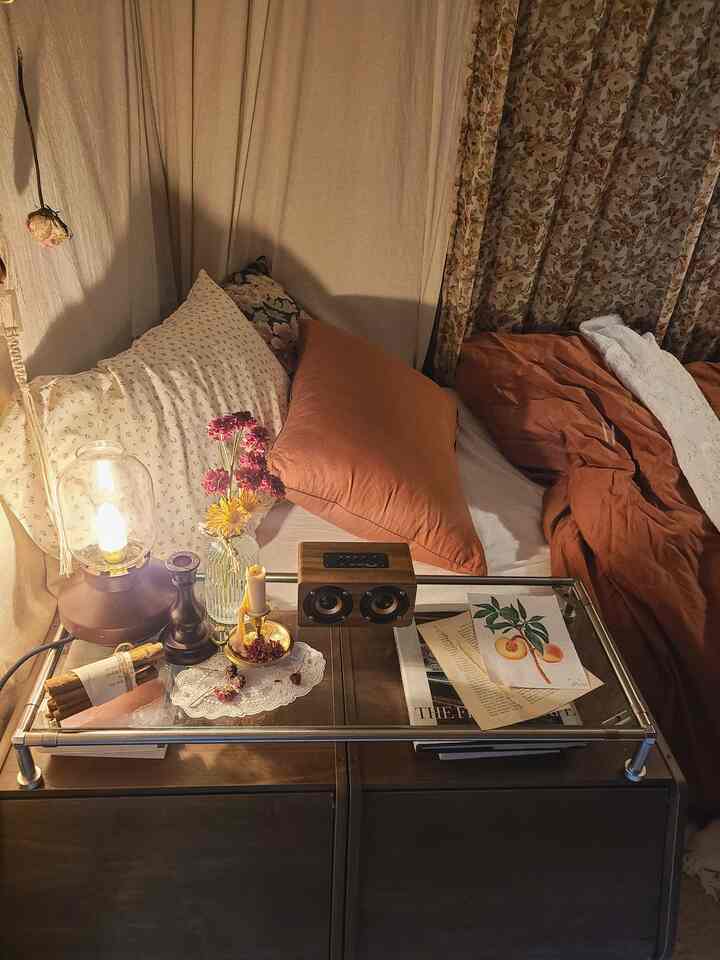 温かみのあるオレンジとナチュラルな色調の寝室、ガラス天板のナイトテーブルとヴィンテージ装飾品が配置された雰囲気のあるインテリア