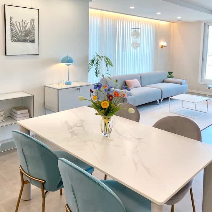 Modern and tidy living room with white and light gray tones featuring a ceramic dining table and sofa