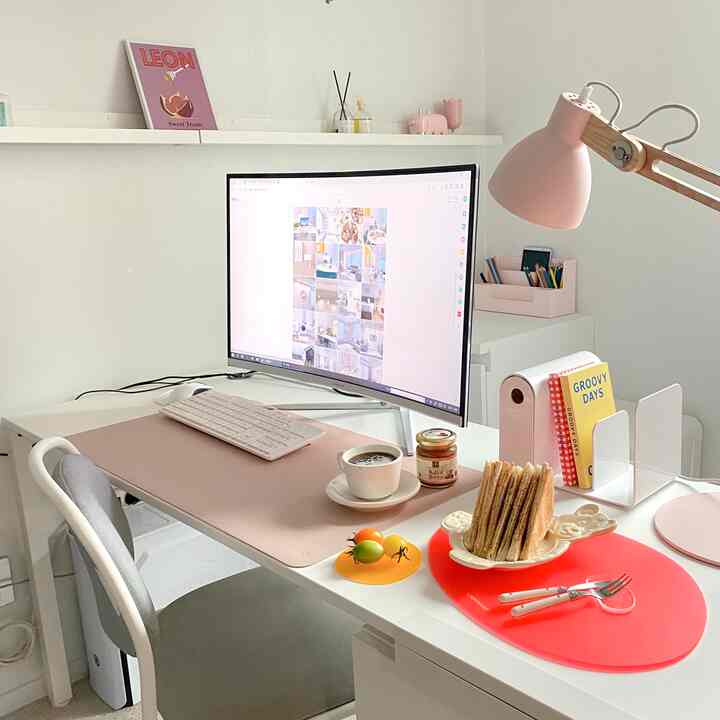 White and pink toned home office space featuring desk and curved monitor with a clean, simple work setup