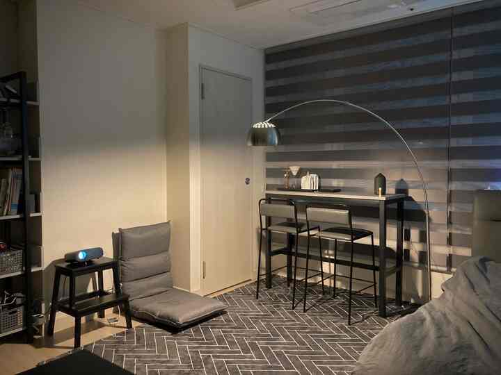 Gray monotone living room featuring a floor chair, projector, bar stools, and steel floor lamp creating a cozy home cinema space