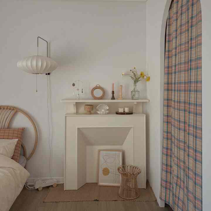 White walls and fireplace with natural rattan furniture and patterned curtain covering arched walk-in closet entrance in cozy bedroom