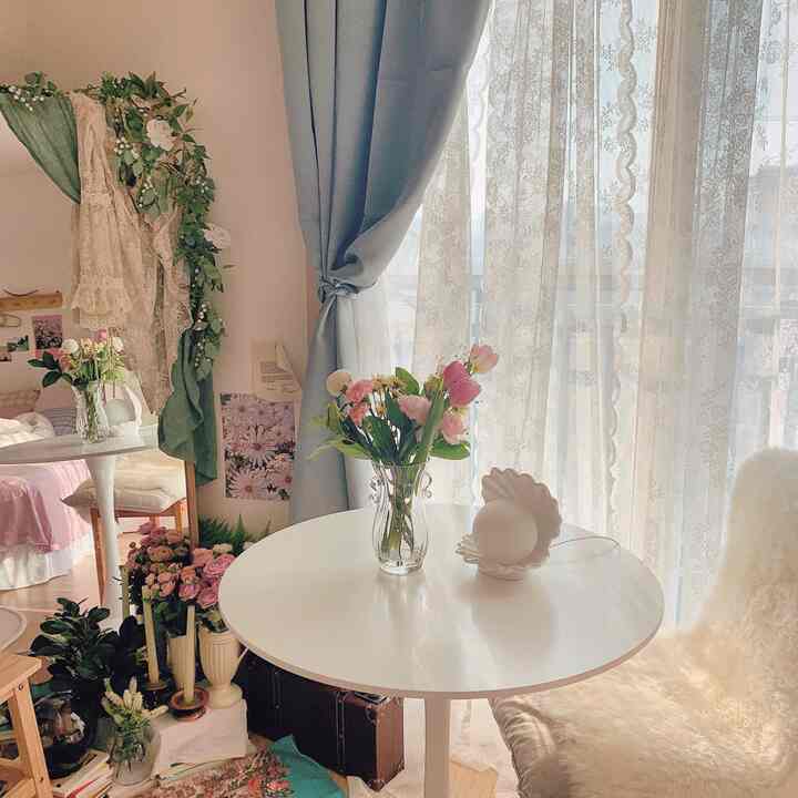 柔らかなパステルトーンとホワイトの丸テーブル、花瓶、全身鏡、シープスキンラグが調和する明るくナチュラルなリビング