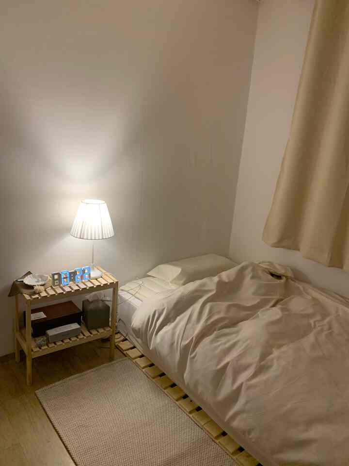 Natural wood tones and beige single bedroom featuring a simple bed, nightstand, and warm lighting creating a cozy ambiance