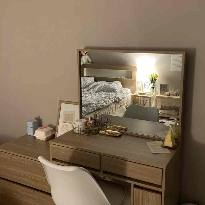 ベージュの壁とナチュラルカラーの寝室の化粧台、白い椅子と額縁が配置された清潔感のある空間