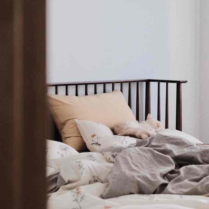 A soothing beige and brown toned bedroom featuring a wooden bed with floral bedding and a sleeping cat, creating a cozy atmosphere